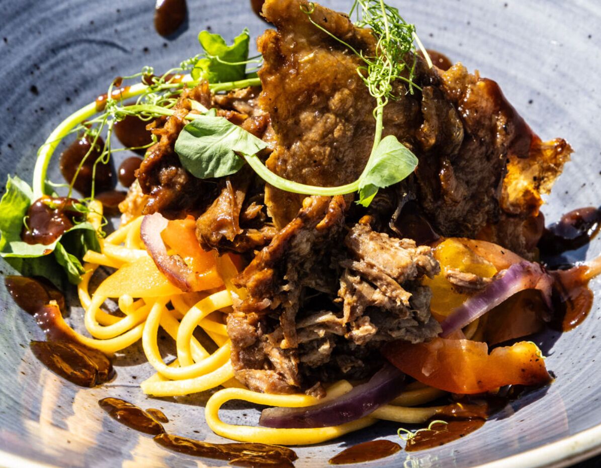 A dish with shredded meat, vegetables, and pasta on a plate.