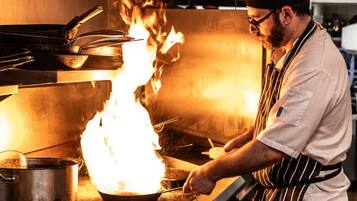 Un chef cocina con una llama grande en una estufa en una cocina profesional.