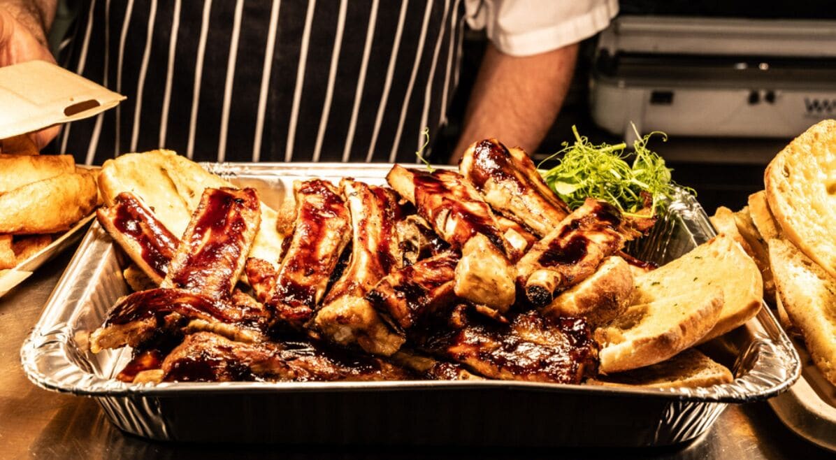 A tray of barbecued ribs and toasted bread on a table.