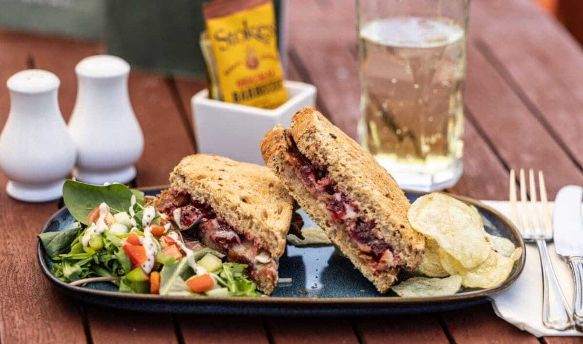 A sandwich cut in half, a salad, chips, and a bottle of beer on a wooden table.