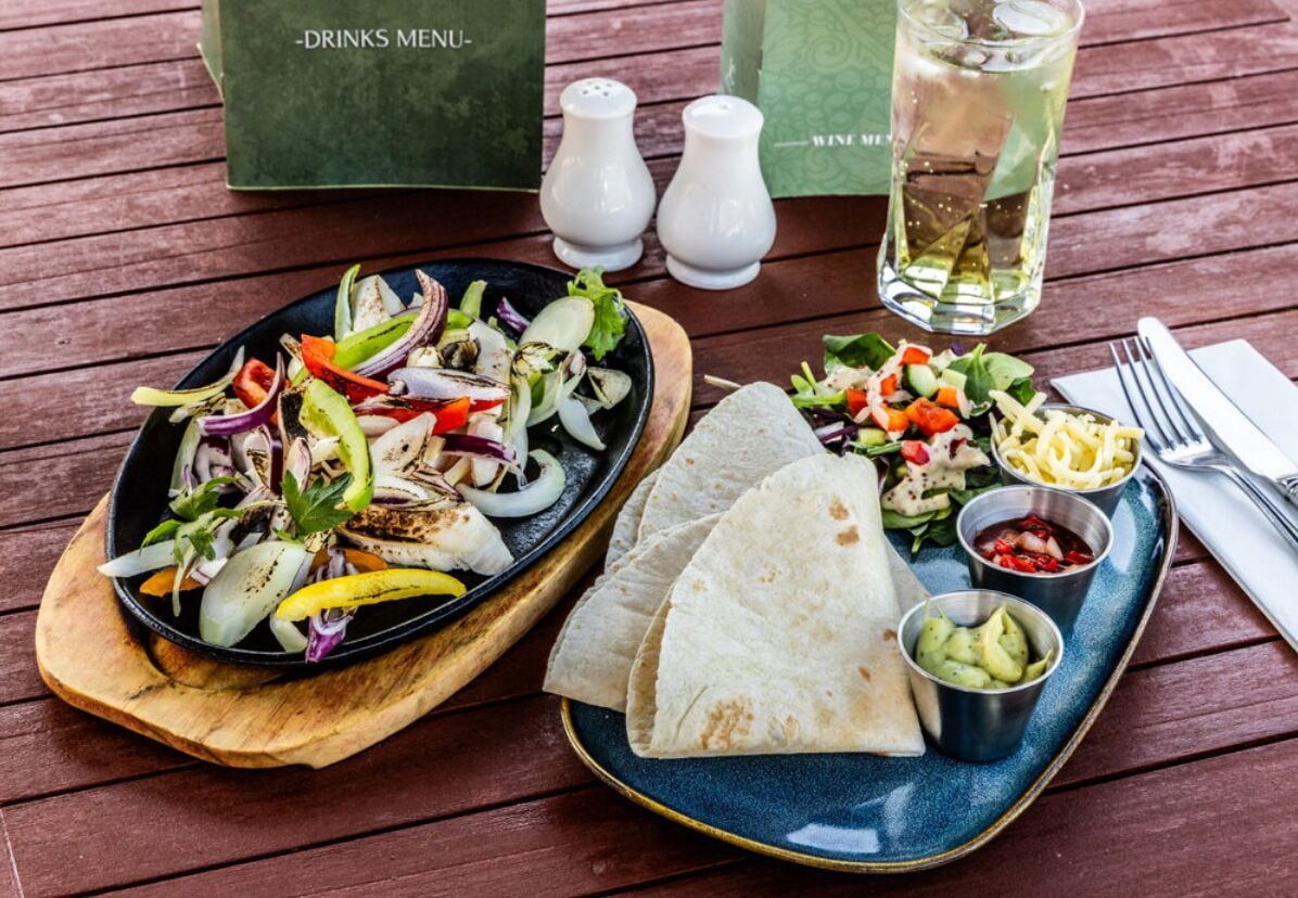 Un plat amb amanida, tortillas i salses sobre una taula de fusta.