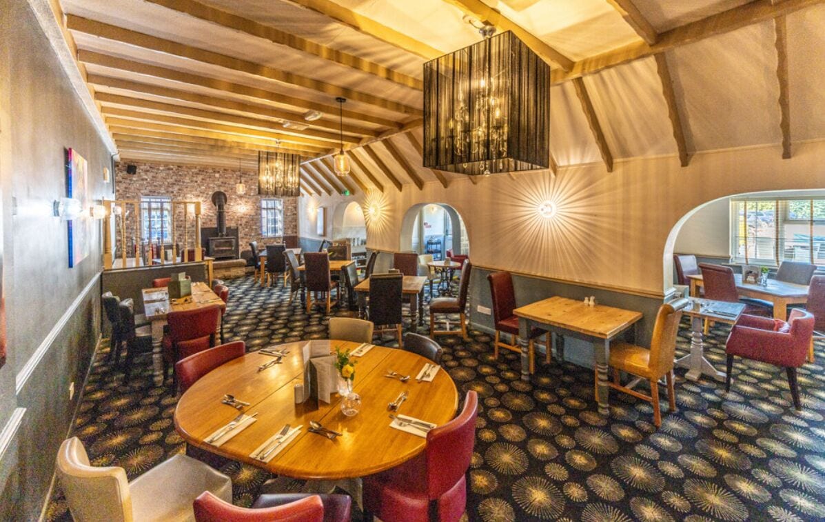 Een restaurant met ronde tafels, rode stoelen en een kamerbreed tapijt met patroon.