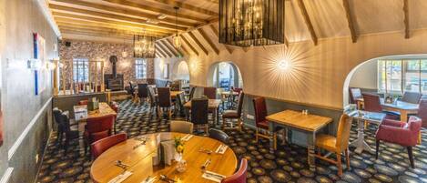 A restaurant with round tables, red chairs, and a patterned carpet.