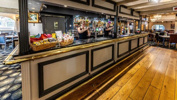 A bar area with a long counter, bar stools, and a variety of bottles and glasses. - The Boars Head Hotel (Ashbourne)