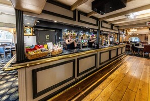 A bar area with a long counter, bar stools, and a variety of bottles and glasses. - The Boars Head Hotel (Ashbourne)