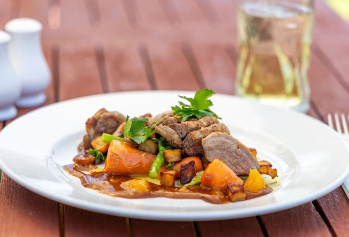 Prato de comida com carne e legumes sobre uma mesa de madeira.