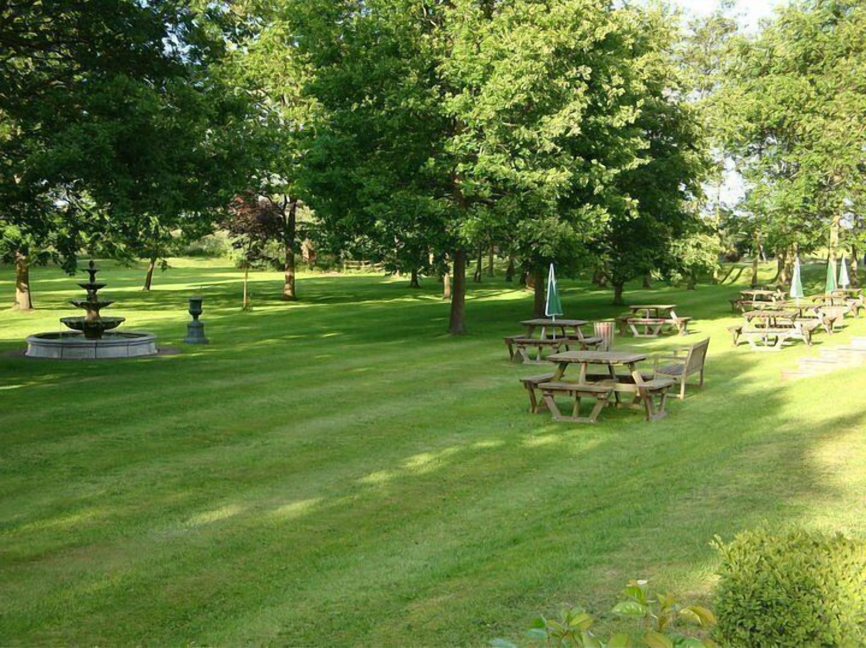 A park with a fountain, picnic tables, and umbrellas.