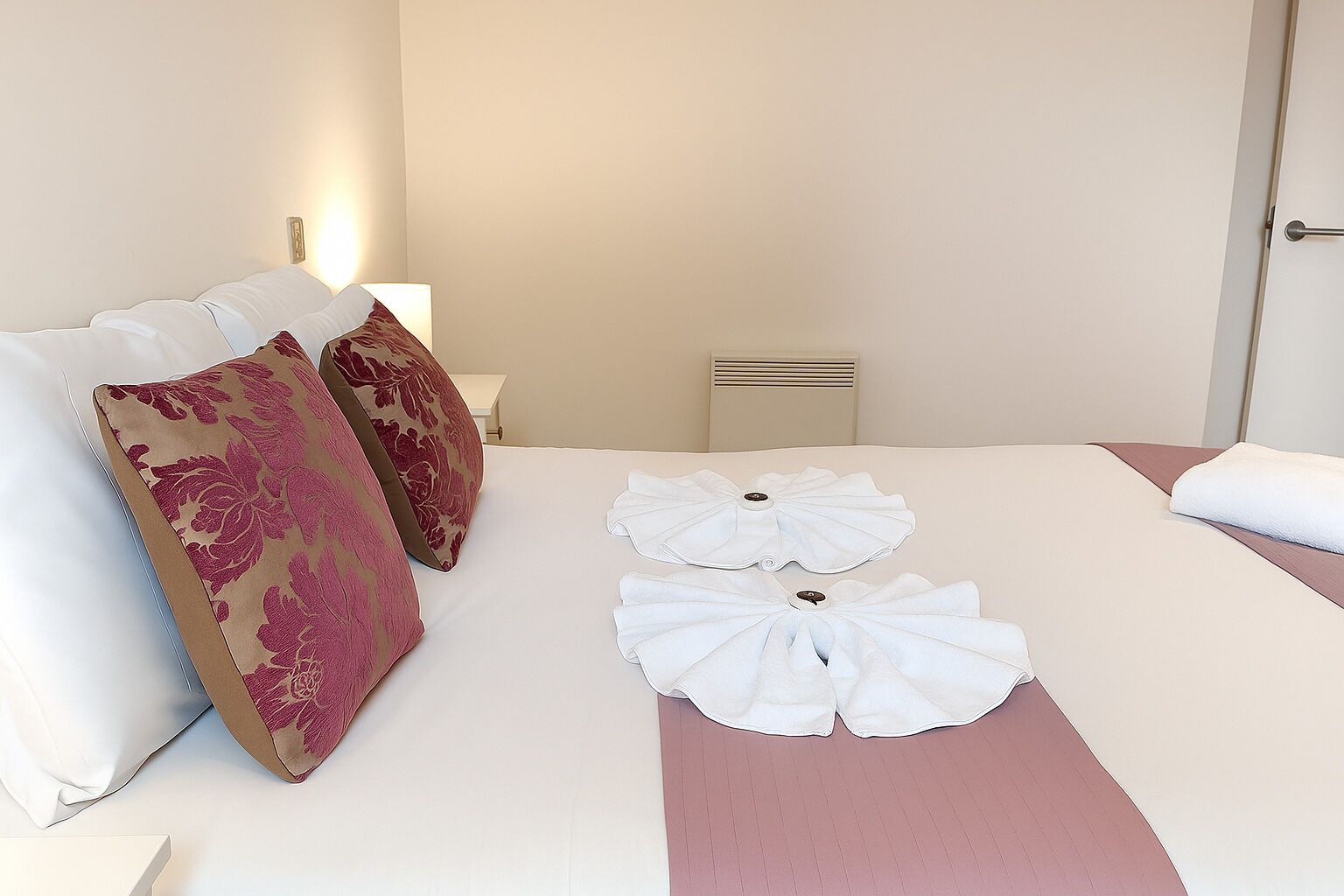 Una habitación de hotel con cama, dos almohadas, una mesita de noche y un buró.