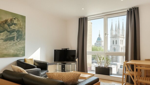A modern living room with a leather sofa, a flat-screen TV, and a dining area with a wooden table and chairs. A large window offers a view of a historic building. - Still Life St. Paul's Executive (London)