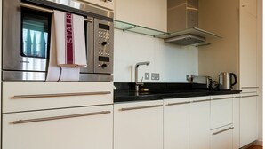 A modern kitchen with white cabinets, stainless steel appliances, and a glass shelf above the counter. - Still Life St. Paul's Executive (London)