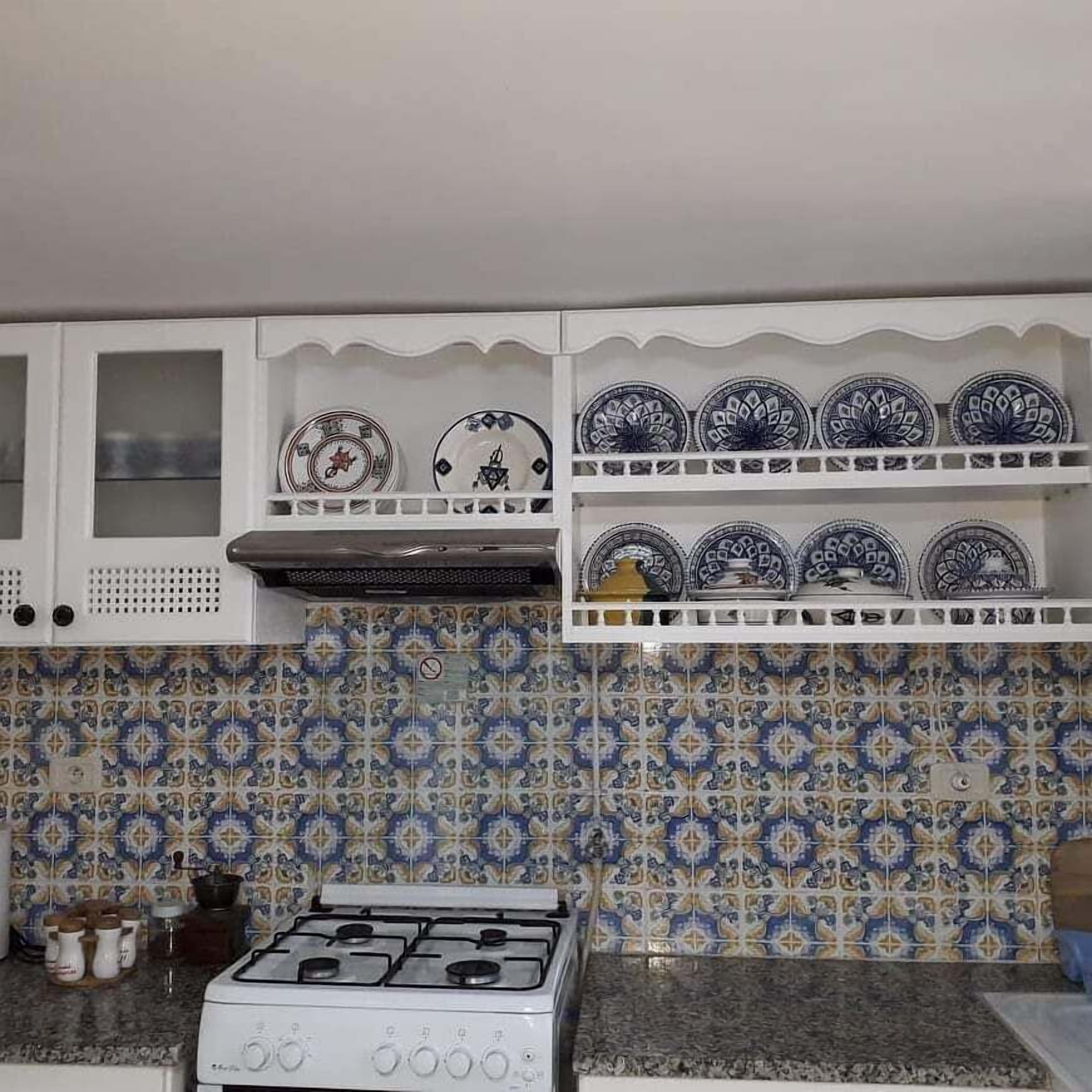 A kitchen with a gas stove, white cabinets, and blue and white patterned tiles.