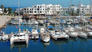 A marina with numerous boats docked, surrounded by white buildings with balconies and a clear blue sky. - Dar El Goulli (Sousse)