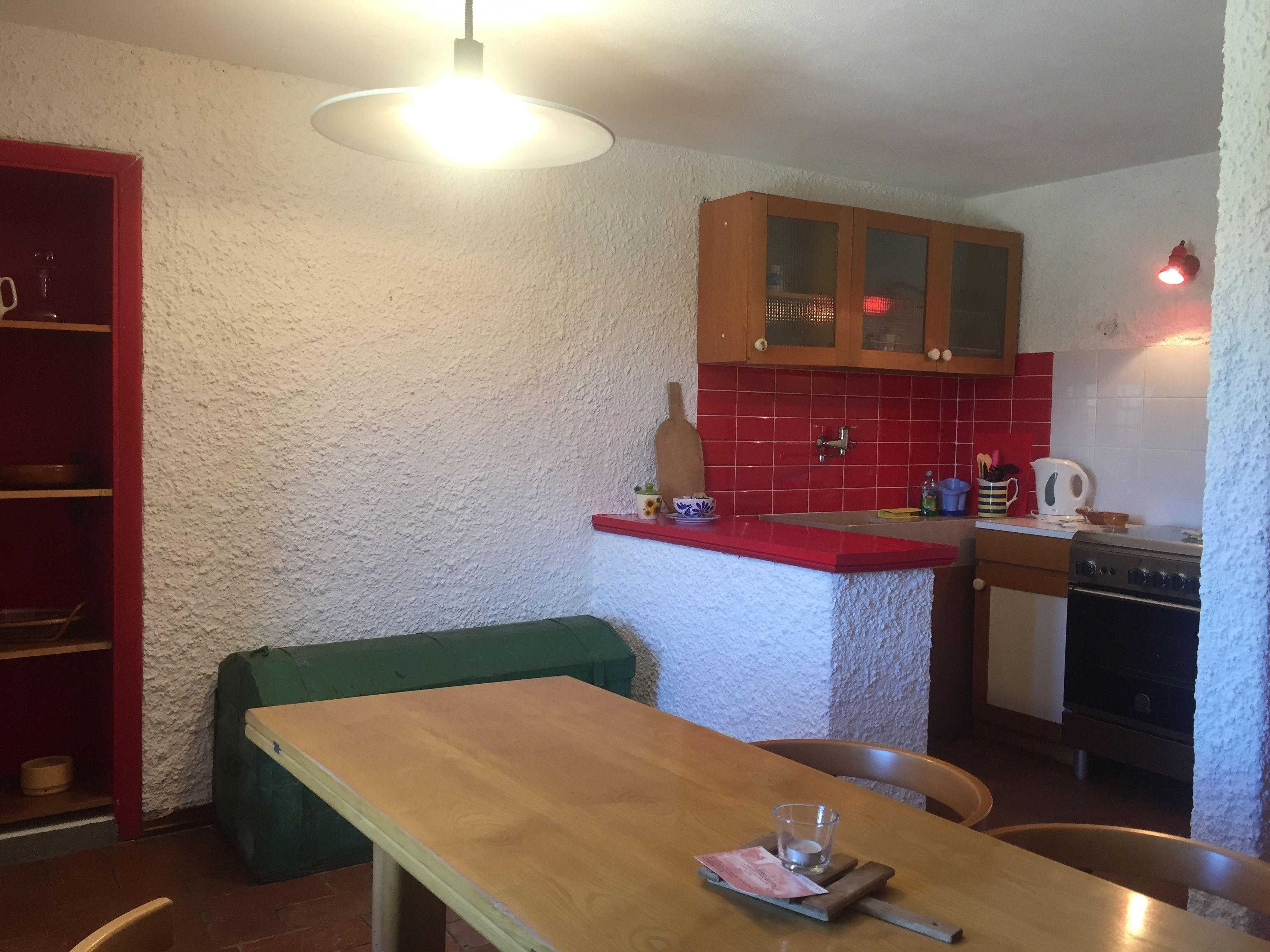 A compact kitchen with a wooden table, a red countertop, and a stove.