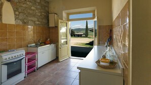 A kitchen with a stone wall, a view through an open door to the outdoors, and a sink with a dish rack. - Agriturismo La Valentina Nuova (Orbetello)