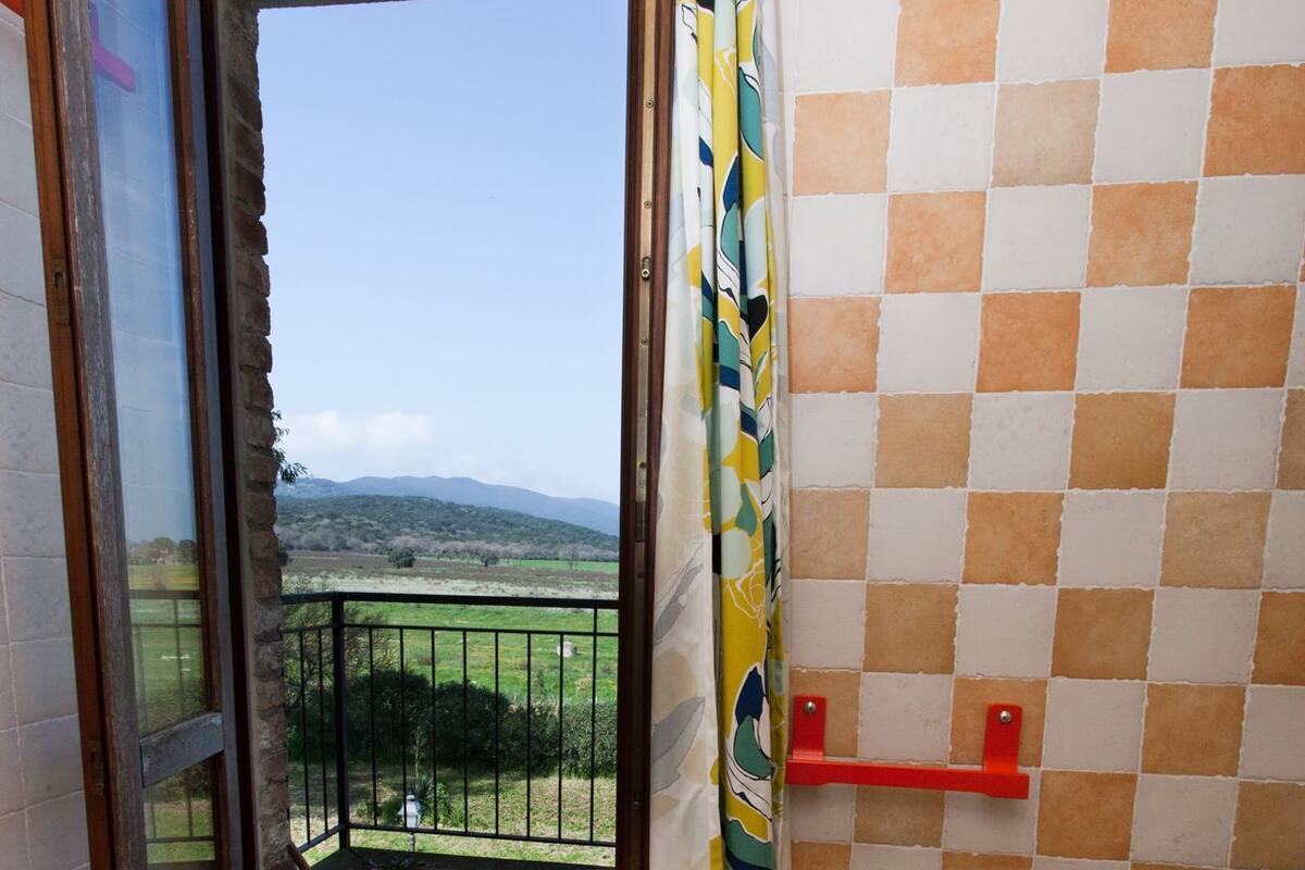 A bathroom with a toilet, a bidet, and a view of a balcony with a railing.
