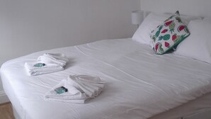 A neatly made bed with white linens and two towels, a patterned pillow, and a white wall with a vent. - Matlaide Superior Apartments (London)