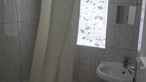 A bathroom with a shower, a sink, and a window with a leaf pattern. - Matlaide Superior Apartments (London)