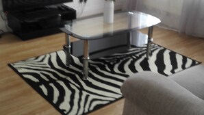 A living room with a flat-screen TV, a glass-top coffee table, a white vase with flowers, a zebra-patterned rug, and a grey sofa. - Matlaide Superior Apartments (London)