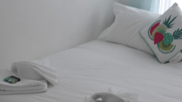 A neatly made bed with towels folded on it, a pillow with a fruit design, and a wooden floor. - Matlaide Superior Apartments (London)