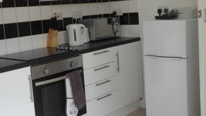 A kitchen with white cabinets, a black countertop, a stove, a microwave, and a refrigerator. - Matlaide Superior Apartments (London)
