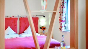A bed with red bedding and white pillows, a vase with flowers, and a bottle on a bedside table. - Hotel Gräffs-Mühle (Traben-Trarbach)