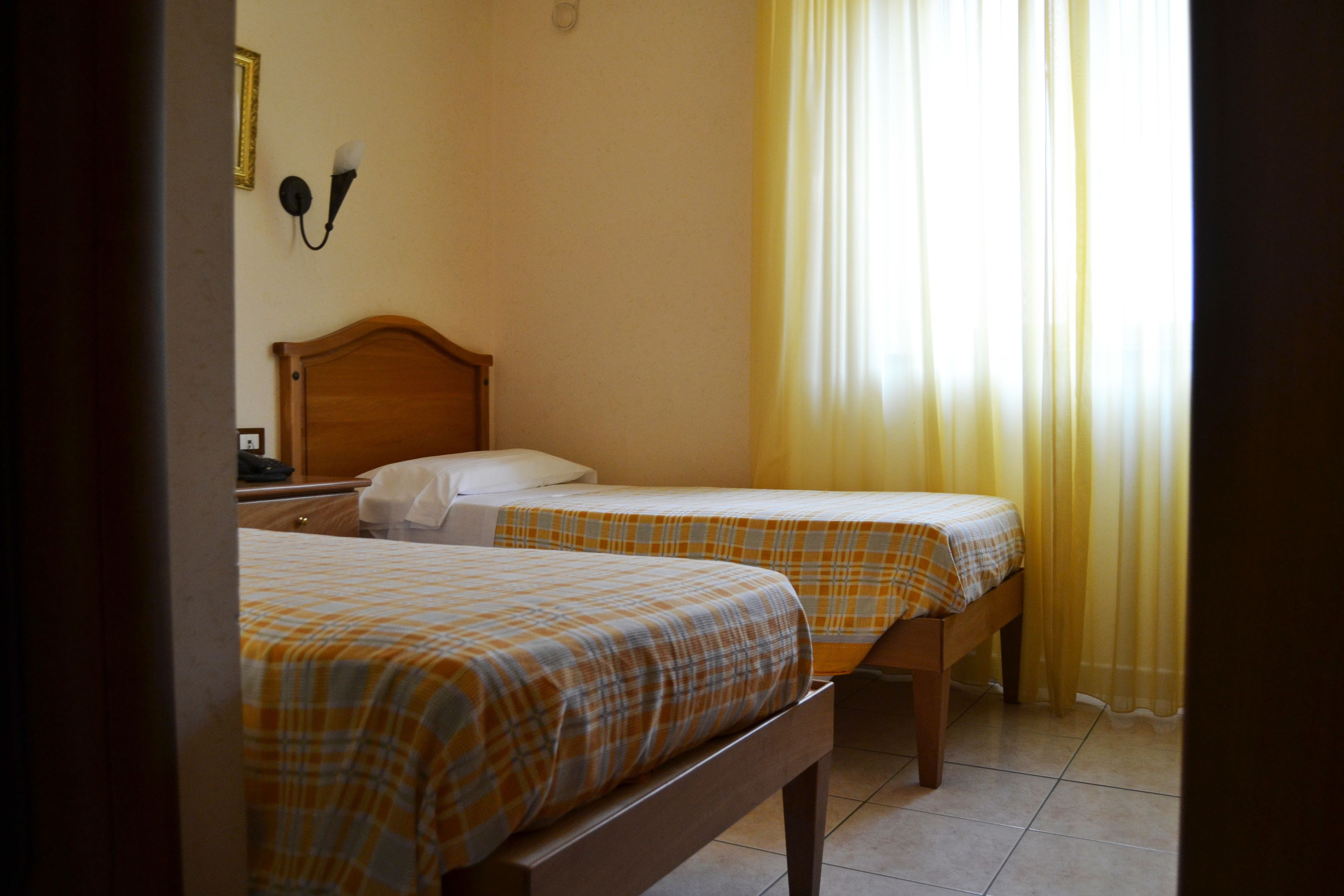 A room with two beds, each with a plaid bedspread, a wooden headboard, and a nightstand with a lamp.