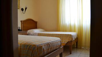 A room with two beds, each with a plaid bedspread, a wooden headboard, and a nightstand with a lamp.