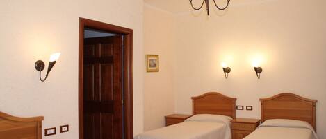 A bedroom with two wooden beds, a wooden wardrobe, a bedside table, a nightstand, a chandelier, and a door.