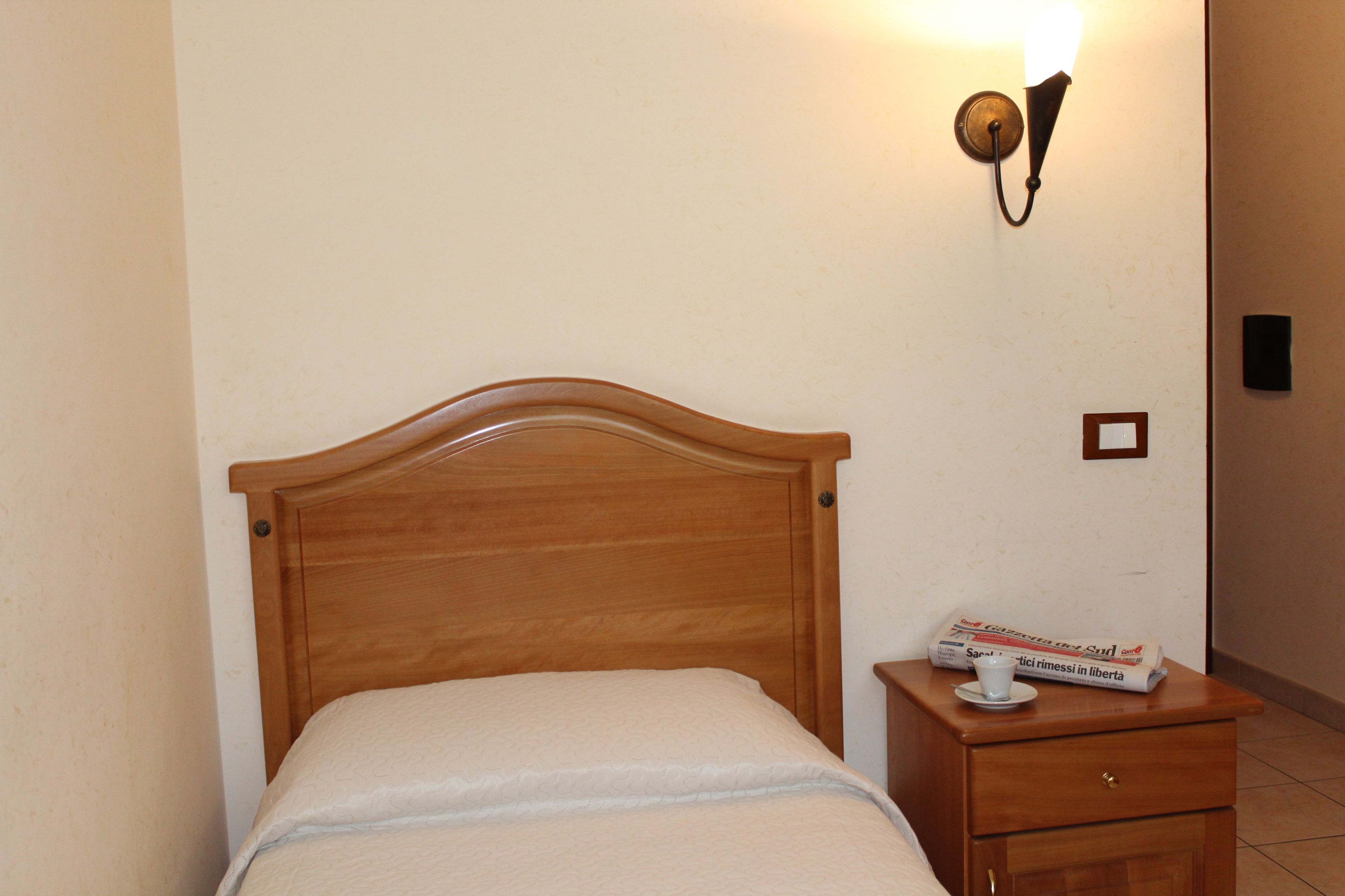 A neatly made bed with a wooden headboard, a bedside table with a lamp, and a newspaper on the table.