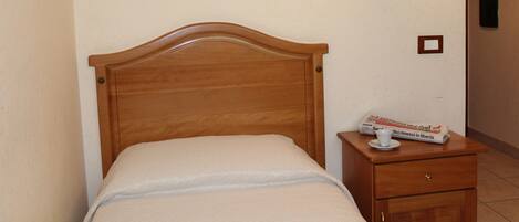 A neatly made bed with a wooden headboard, a bedside table with a lamp, and a newspaper on the table.
