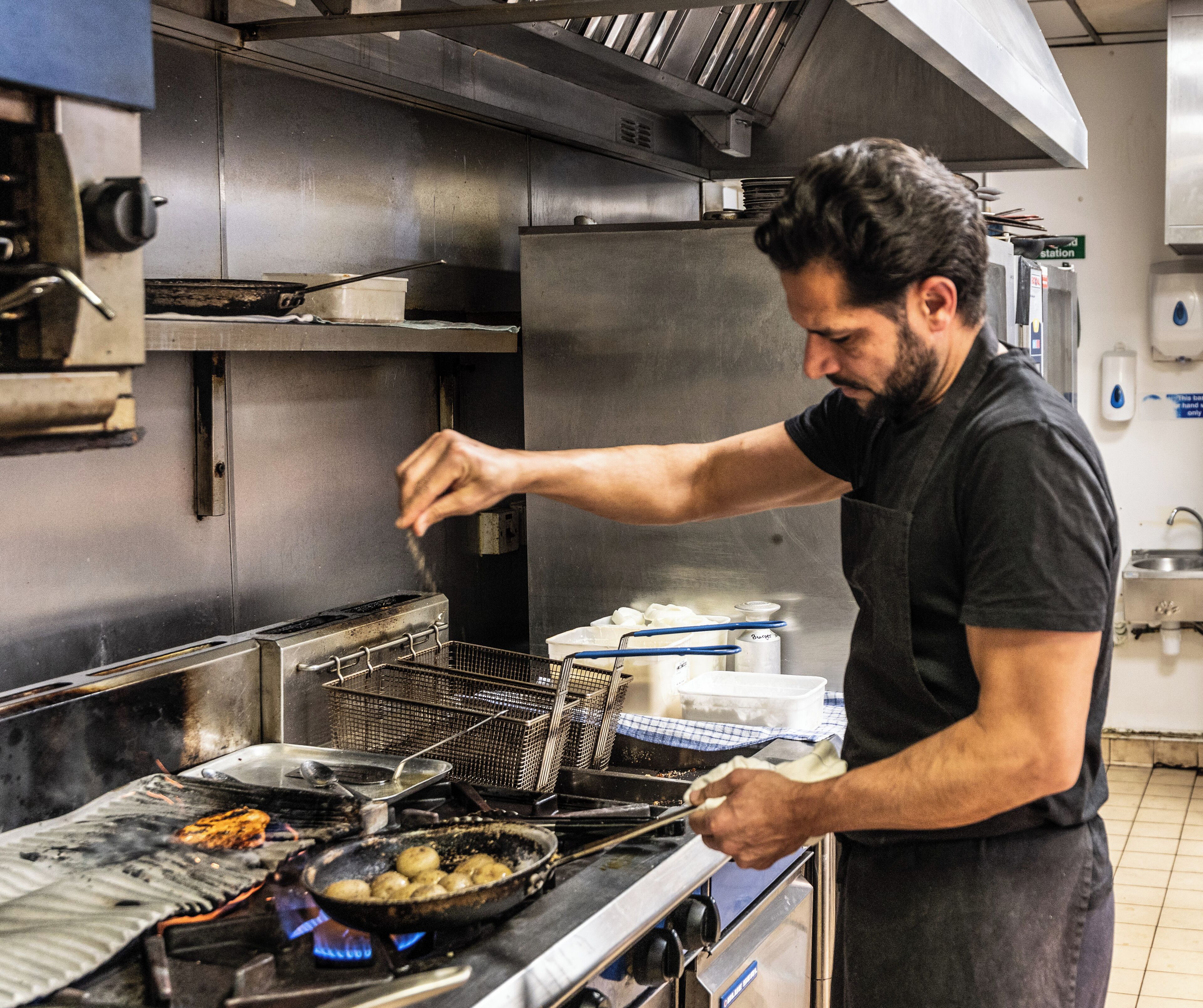 Un chef cuisinant dans une cuisine professionnelle équipée d’appareils en acier inoxydable et dotée d’un mur recouvert de carreaux.