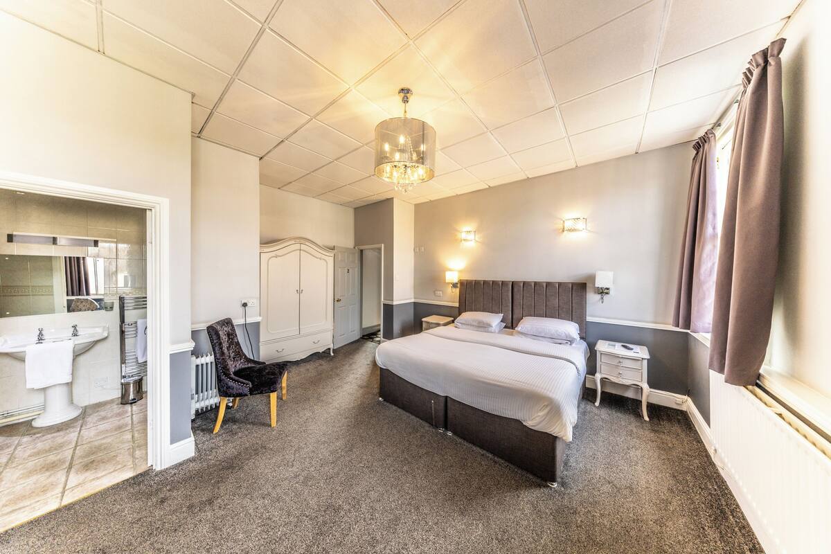 A hotel room with a large bed, bedside tables, a vanity with a mirror, and a chandelier.