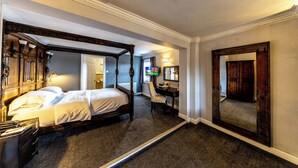Een hemelbed, een bureau met stoel, een televisie en een grote spiegel in een hotelkamer.