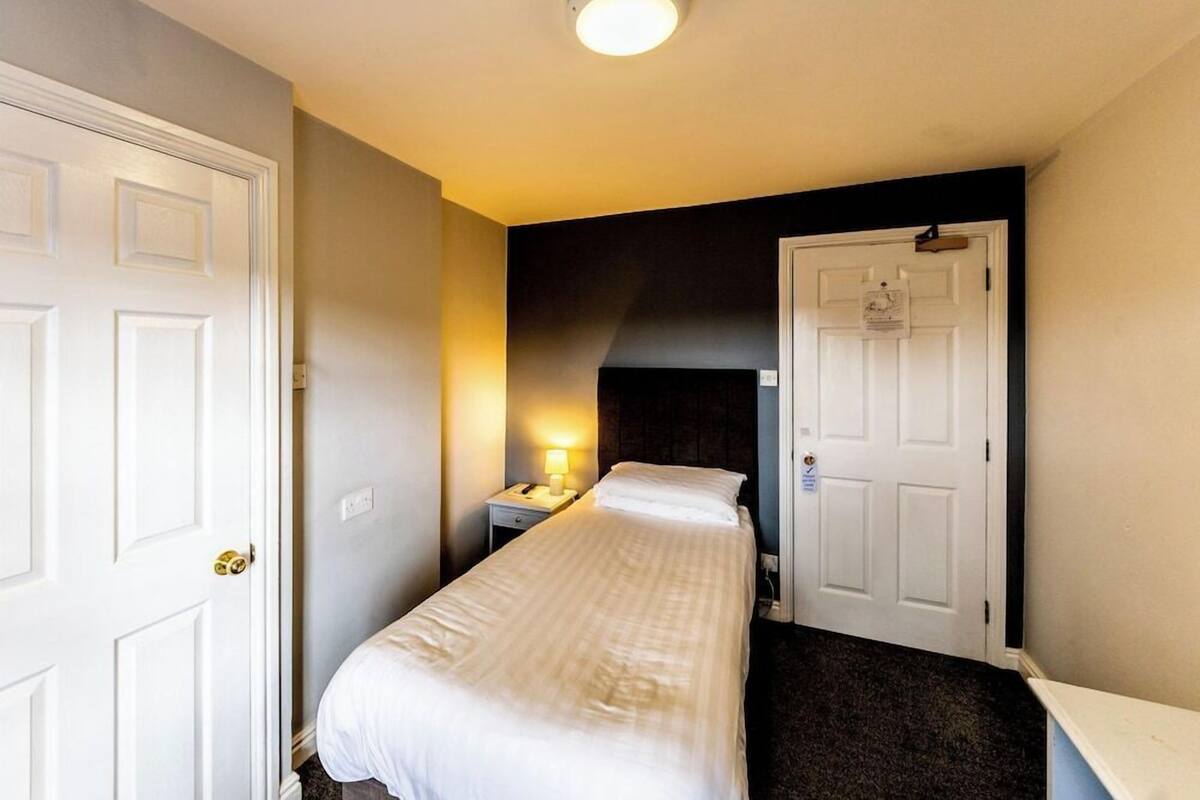 A hotel room with a single bed, a nightstand with a lamp, and a door with a sign.