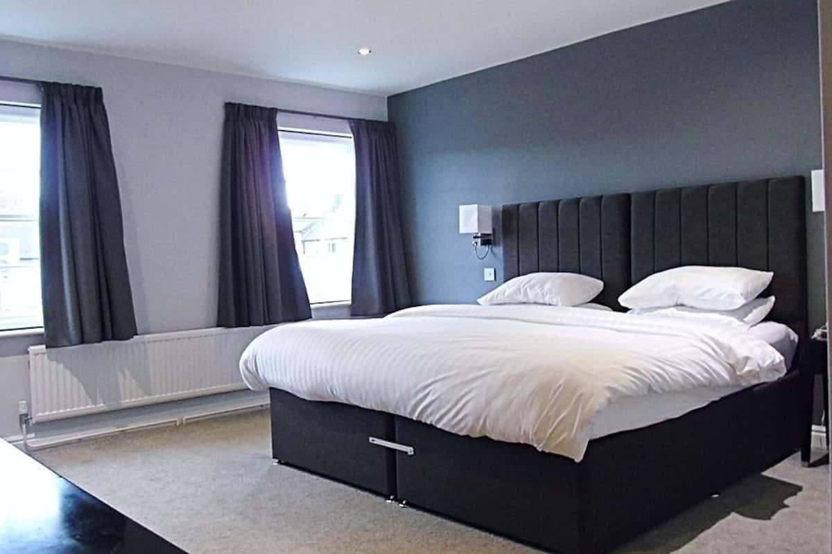 A modern hotel room with a large bed, a nightstand, a window with curtains, and a radiator.
