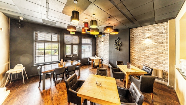 Een restaurantinterieur met houten tafels en stoelen, bakstenen muren en hangende吊り下げ照明.