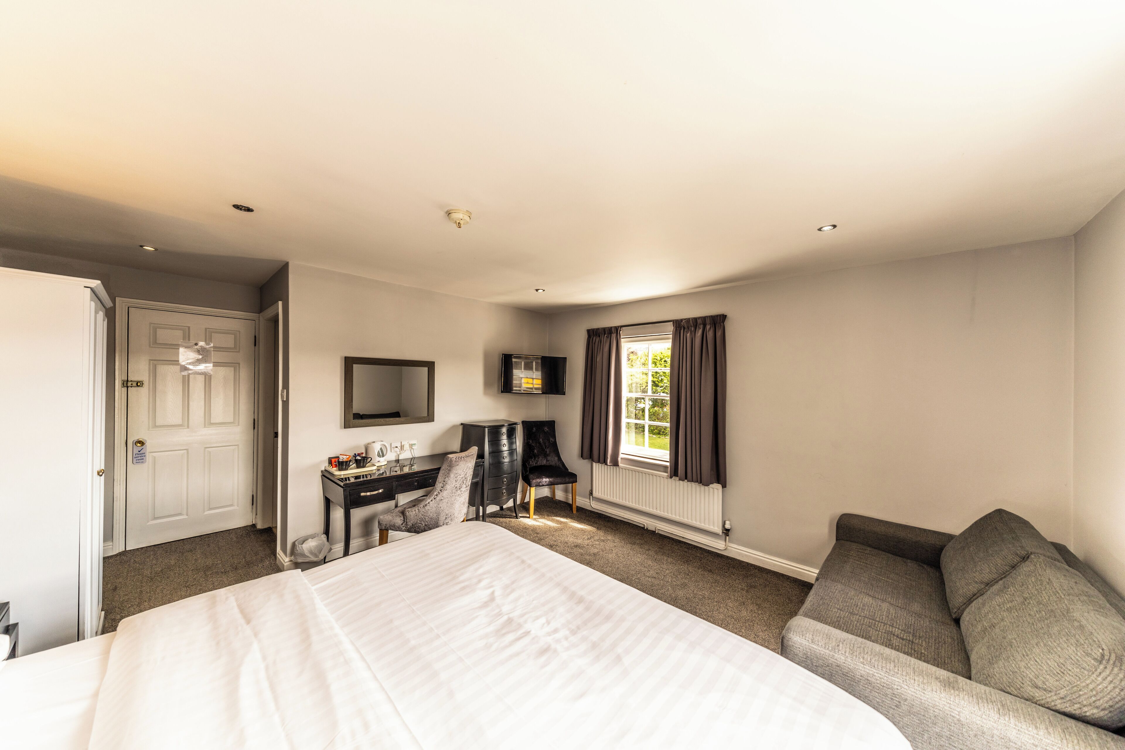 A hotel room with a large bed, a desk with a chair, a television, and a window with curtains.