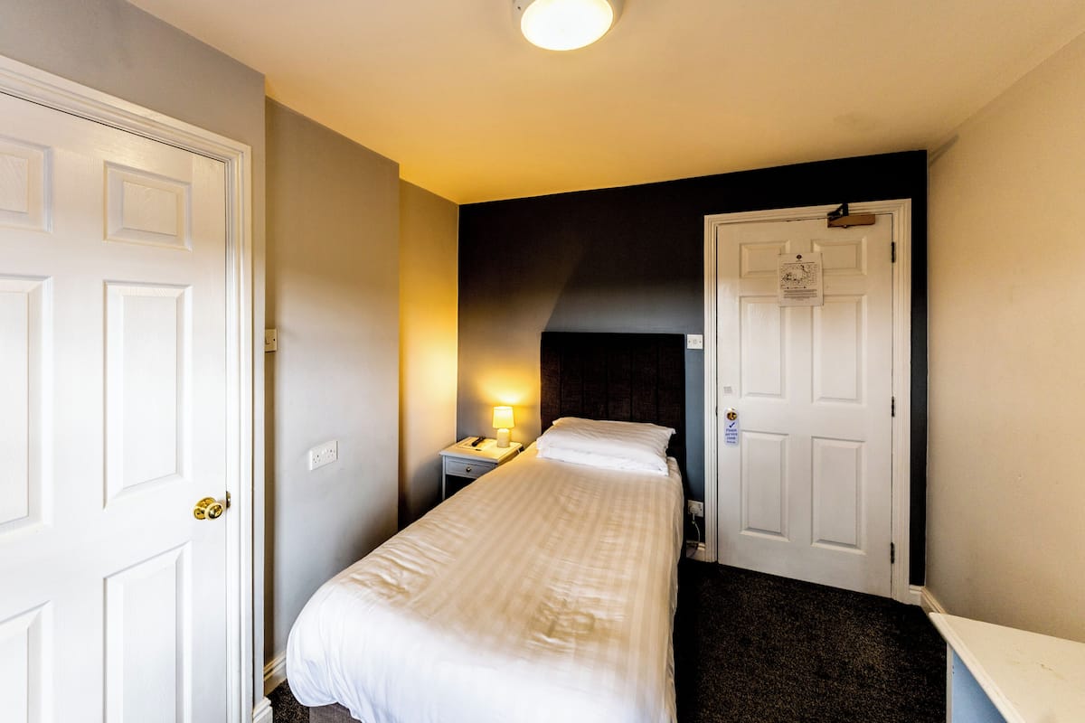 A hotel room with a bed, a nightstand with a lamp, and a door.