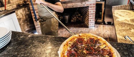 A pizza in a kitchen with a brick oven in the background.