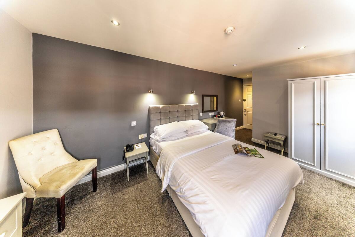 A hotel room with a large bed, a chair, a nightstand, a wardrobe, and a mirror.
