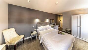 A hotel room with a large bed, a chair, a nightstand, a wardrobe, and a mirror.