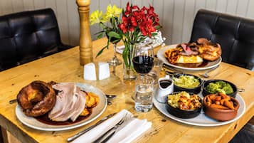 A dining table with a variety of dishes, including a roasted turkey, Yorkshire pudding, and several side dishes. There are salt and pepper shakers, a vase with flowers, and a glass of red wine.