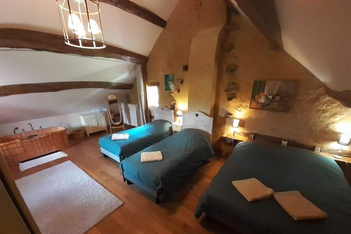 A cozy bedroom with two beds, a wooden bathtub, and a rustic stone wall.