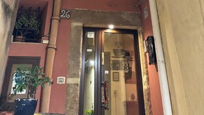 A building with a balcony, a door with a sign, and a potted plant. - La Corte Normanna (Sciacca)