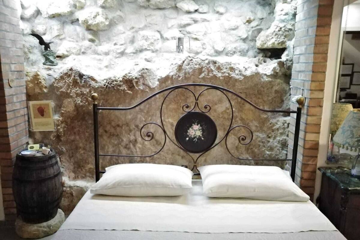 Una cama con cabecera de metal en una habitación con pared de piedra.