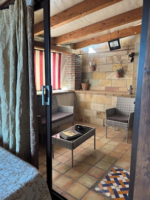 Una habitación con puerta de vidrio, mobiliario de mimbre, pared de ladrillo y suelo de baldosas.