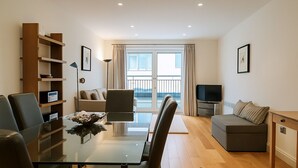 Ein modernes Wohnzimmer mit einem Glastisch, Ledersesseln, einer Couch, einem Fernseher und einem Balkon mit Vorhängen.