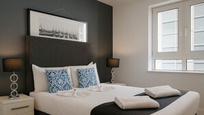 Ein modernes Schlafzimmer mit einem großen Bett, zwei Nachttischen, einem gerahmten Bild über dem Bett und einem Fenster mit Jalousien.