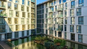 A modern building with multiple floors, large windows, and a central courtyard with a water feature and greenery.