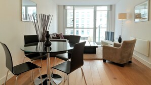 A modern living room with a round glass table, black chairs, a beige sofa, and a TV.